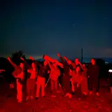 Participants at a nighttime star party using a telescope under red-light conditions
